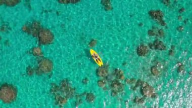 Sarı bir kanoyla turkuaz suda kürek çeken bir kadının, resifleri ve tropikal denizlerdeki gizli plajları keşfettiği hava aracı görüntüleri.