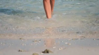 Kaygısız kadın, turkuaz okyanusun kenarında güneşli bir yaz gününün tadını çıkararak, beyaz bir kumsalda yalınayak yürüyor.