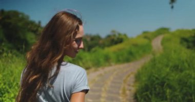 Uzun saçlı bir kadın Ubud, Bali 'de toprak yolda yürüyor. Yavaş çekim, Campuhan Tepesi Yürüyüşü boyunca hareketlerini yakalıyor..