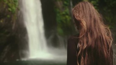 Sinema ağır çekim orman şelalesi. Uzun saçlı kadın, egzotik yağmur ormanlarındaki yüksek şelaleli tropik ada manzarasının tadını çıkarıyor. Bali Endonezya. Yaz tatilindeki bir kadın. Arka planı kapat