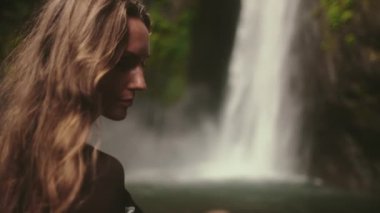 Güçlü Bali şelalesine karşı duran uzun saçlı kadın. Seyahat, turizm, tatil, özgürlük ve aktif yaşam tarzı konsepti. Endonezya, Bali adası, Air Terjun Munduk, Melanting Waterfalls. Yavaş çekim