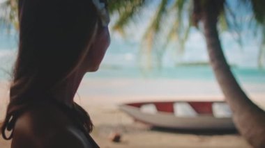 Saçında frangipani çiçeği olan genç bir kadın tropik bir sahil manzarasının tadını çıkarıyor, mutlu ve rahat hissediyor.