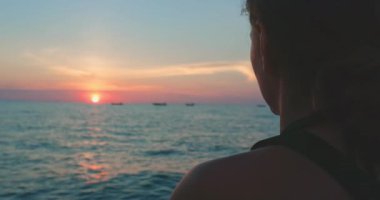 Tayland 'da bir tekne turunda okyanusun kenarında duran bir kadın gün batımını seyrediyor. Arka planda dalgalar çarpışıyor..