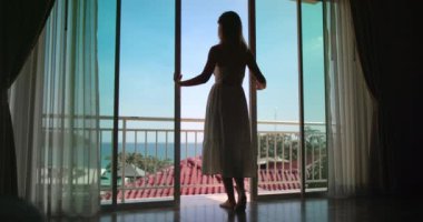 Turist otel odasının terasına giriyor ılık yaz melteminin ve balkonunun güzel manzarasının tadını çıkarıyor.