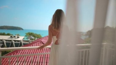 Kadın, tropik ada manzarası, Phuket, Tayland 'ın tadını çıkarmak için otel odasının terasında yürüyor. Kapı perdeleri rüzgarda savrulur. Yaz tatilinde, lüks bir tatil beldesinde açık havada hayat yolculuğu. Arka plan yavaş çekim