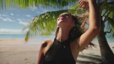 Dalgıç kıyafeti giymiş bir kadın kumlu bir sahilde duruyor, dalgalar arkasına çarpıyor ve okyanus ufka doğru uzanıyor..