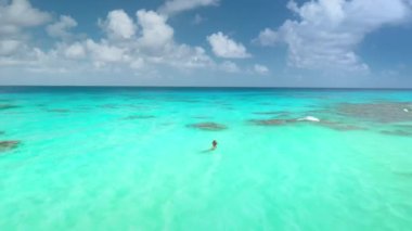 Kristal turkuaz su, tropikal egzotik ada, mavi bulutlu gökyüzü, güneşli gün. Açık deniz mercan kayalıklarında yüzen bir kadın. Yaz tatilinde açık hava seyahati. Panoramik İHA uçuşu