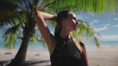 Kadınlar tropik ada plaj manzarasından hoşlanırlar. Siyah bikinili esmer, esmer, beyaz bir kız yeşil palmiye ağacı ve arka planda mavi gökyüzü. Seyahat, turizm, tatil. Ağır çekim. Fransız Polinezyası