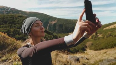 Karpat dağlarında yürüyüş turunda selfie çeken bir kadın. Turist kadın akıllı telefonuyla fotoğraf çekiyor, doğa güzelliğini paylaşıyor. Gezgin tatilini dışarıda geçirir, yürüyüş yapar, spor yapar. Yavaş çekim