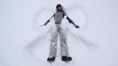 Bir kadın taze karda uzanır, kolları ve bacaklarıyla bir kar meleği yaratır, sakin bir kış manzarasıyla çevrili..