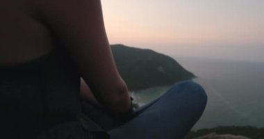 Bir insan bir dağın tepesinde bacaklarını çaprazlayarak oturur ve etrafındaki panoramik manzarayı seyreder..