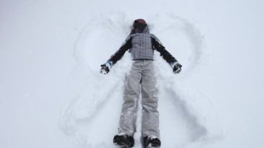 Bir kadın taze karda yatar, soğuk bir kış gününde, sakin karlı bir manzarayla çevrili bir kar meleği yaratır..