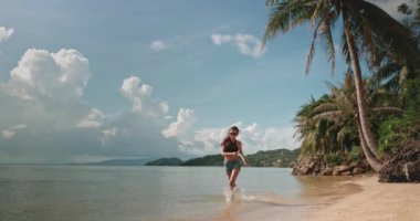 Tayland 'daki Koh Phangan tropikal adasında kumsalda ağır çekimde koşan güzel bir kadın. Okyanus dalgaları kıyıya değiyor. Yaz tatilinde açık hava seyahati