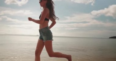 Tayland 'daki Koh Phangan tropikal adasında kumsalda ağır çekim koşan bir kadın. Okyanus dalgaları kıyıya değiyor. Yaz tatilinde açık hava seyahati. Arka plan