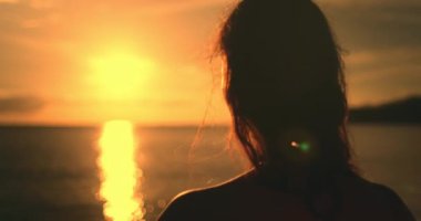 Kadın yüzünü parlak turuncu günbatımına yakın tut. Kız silueti, tropikal bir plajda durup turuncu dramatik gökyüzüne ve okyanus dalgalarına karşı inanılmaz renkli günbatımının keyfini çıkarıyor. Tatil seyahati