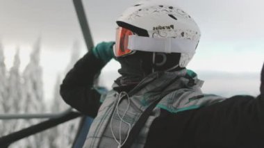 Kask takan ve gözlük takan kayakçı heyecan içinde kollarını kaldırarak karlı bir dağın tepesine tırmanırken kayak asansörüne biner.