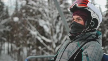 Mutlu kadın, kar ve ağaçlarla dolu huzurlu kış manzarasında kayak asansörüne biniyor. Kayak merkezinde çok soğuk bir günde kar yağarken klasik bir teleferikle. Bukovel Dağları, Ukrayna