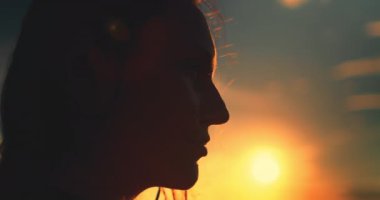 Gün batımına karşı kadın silueti parlak turuncu gökyüzü. Kız elini kaldırır ve güzel doğa manzarasının tadını çıkarır. Yaz tatilinde açık hava seyahati. Yavaş çekim geri görünümü