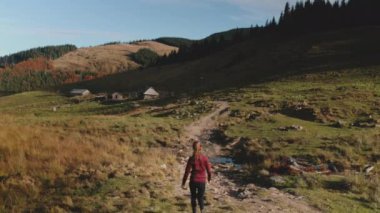 Turist kadın kırsal dağ yolunda yürüyor. Sonbahar çayırlığı manzarası, çam ağacı ormanı, eski ahşap çiftlik evleri. Yaz tatilindeki kadın turist. Yaşam tarzı tatil konsepti. Karpatlar