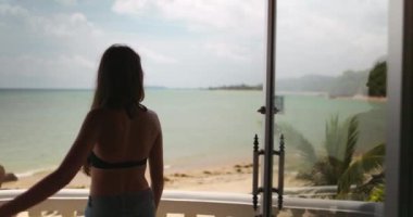 Genç bayan Tayland 'da güzel bir plaja bakan bir terastan manzaranın tadını çıkarıyor. Videonun yavaş çekim etkisi var.