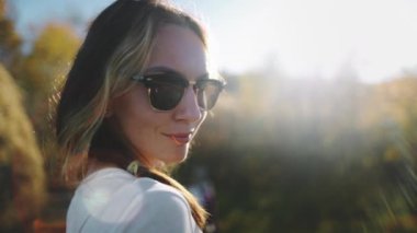 Gün batımında kadın portresi. Yavaşça gülümseyen, kameraya bakan. Güneş gözlüklü genç bayan rahatla, hayatın tadını çıkar, eğlen, dinlen, meditasyon yap. Tatilde aktif yaşam tarzı seyahati