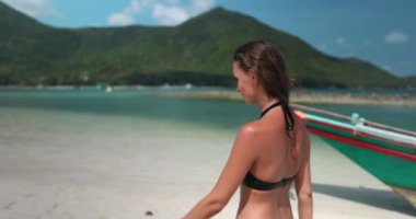 Bikini giyen bir kadın parlak güneşin altında Tayland 'da kumlu sahilde yürüyor. Dalgalar arka planda dönüyor, sıcak havanın tadını çıkarıyor. Rahatlayın, açık hava gezisi, yaz tatili