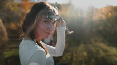 Güneş gözlüğü takan kadın gün batımı doğa manzarası. Kırsal kırsal sonbahar manzarasından hoşlanan bir kız. Genç bayan rahatla, dinlen, meditasyon yap. Tatilde aktif yaşam tarzı seyahati. Yavaş çekim
