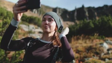 Selfie çekmek için elinde cep telefonu tutan aktif bir turist kadın. Arka planda dağ doğası manzarası. Beyaz kız yürüyüşçülerin hoşuna gider. Seyahat, turizm, tatil, yürüyüş, yürüyüş, aktif yaşam tarzı