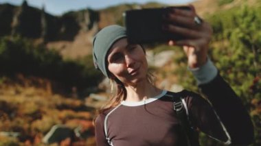 Genç bir kadın cep telefonuyla canlı bir dağ manzarası selfie 'si çekiyor. Aktif turist fotoğraf çekiyor. Beyaz kız yürüyüşçülerin hoşuna gider. Seyahat, turizm, yürüyüş, yürüyüş, aktif yaşam tarzı