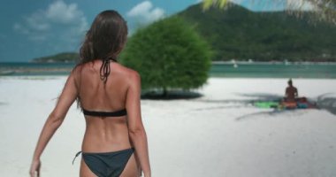 Genç bir kadın Tayland 'da güzel bir tropikal sahilde güneşli bir günün tadını çıkarıyor. Beyaz kumda yürüyor ve turkuaz suya yaklaşıyor.