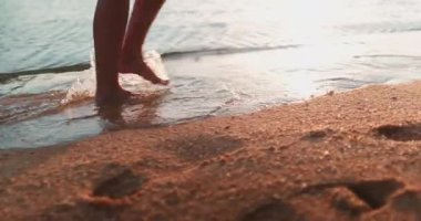 Günbatımı kumlu sahilde gezinen biri. İnce kadın bacakları okyanus suyunun kumsalında yürüyor. Gün ışığında deniz kenarında sörf yapan çıplak ayaklı bir kadın. Yaz tatilindeki kız turist tropik ada beldesinde.