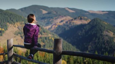 Turist dişiler Karpat Dağları 'nın tadını çıkarırlar. Yürüyüş kıyafetleri içinde genç bir kadın ahşap çitlere oturur, güneşli bir günde dinlenir. Seyahat, aktif turizm, tatil, yürüyüş, dinlenme. Arka plan