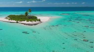Güneşli bir günde, kristal berraklığında turkuaz suyla çevrili, uzak bir adada güneşlenen bir kadının hava görüntüsü.