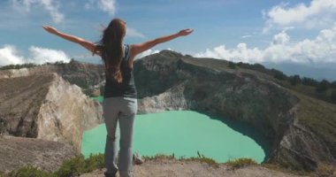 Dişi turist, turkuaz suyla bir krater gölünün kenarında dururken doğanın güzelliğini kucaklıyor. Filipinlerdeki volkan kraterinin manzarasının tadını çıkarıyor.