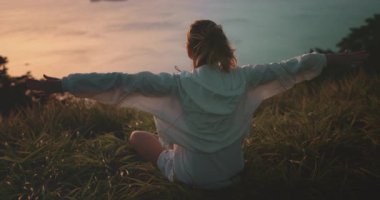 Genç bir kadın gün batımında bir tepede meditasyon yapıyor ve yoga yapıyor. Kendini özgür ve doğaya bağlı hissediyor.
