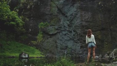 Etrafı sarp kayalıklarla çevrili tropik bir şelalede doğanın tadını çıkaran bir kadın huzur cenneti yaratıyor.