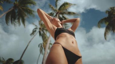 Bikinili tasasız bir kadın tropik bir plajda güneşin tadını çıkarıyor. Cennette özgürlük ve rahatlığın vücut bulmuş hâli.