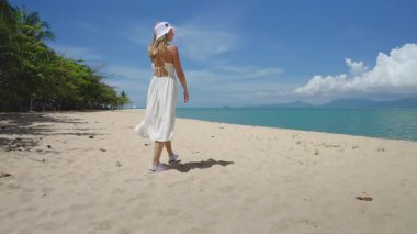 Beyaz elbiseli bir kadın vahşi tropik kumsalda yürüyor. Yaz tatilinde açık hava seyahati. Kafkas dişileri rahatlar, vahşi ada doğasının tadını çıkarırlar. Parlak güneşli bir gün, mavi gökyüzü. Arka plan, pov