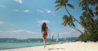 Bikinili bir kadın Boracay Adaları 'nın kumlu sahillerinde koşuyor. Meşhur White Beach, berrak su kenarında güneşli günün tadını çıkarıyor..