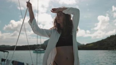 Genç bir kadın neşeli bir şekilde yelkenlide bir halat tutuyor güneşli bir günde sakin denizde yelken açarken rüzgarı yüzünde hissediyor.