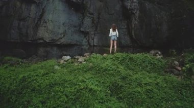 Genç bir kadın tropikal bir adayı keşfediyor, yemyeşil bir bitki örtüsünün kenarında, yüksek bir kaya yüzeyinin yanında duruyor, bu el değmemiş cennette huzur ve özgürlüğü hissediyor.