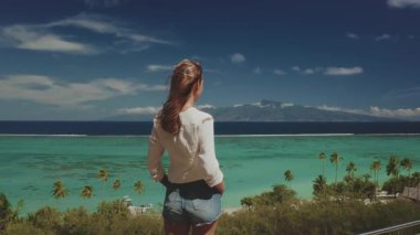 Genç kadın, berrak turkuaz suları, yemyeşil suları ve uzaktaki görkemli dağlarıyla tropikal bir ada cennetinin nefes kesici manzarasını izliyor.