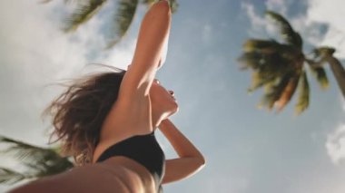 Genç bir kadın tropik bir plajda huzur içinde dinleniyor. Sıcak güneşi ve yumuşak rüzgarı hissetmek. Dalgalı palmiyelerle dolu, parlak mavi bir gökyüzünde tasasız ve mutlu.