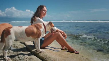 Kayalık sahilde oturan bir kadın köpekle kumsalda rahatlar. Sahilde birbirine sarılıp okyanus dalgalarını seyreden bir köpek. İnsanlar ve evcil hayvanlar hafta sonunun tadını çıkarırlar. Sakin sakin, güzel doğa.