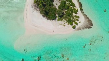 Maldivler içinde beyaz kumsalda yürüyen bir kadının havadan görünüşü turkuaz sular ve palmiye ağaçları lüks bir tatil için bir cennet yaratıyor.