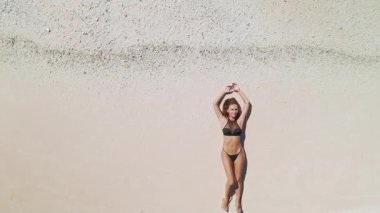 Siyah bikinili bir kadın Maldivler 'de el değmemiş beyaz bir kumsalda sırt üstü yatıyor. Kolları başının üstünde, güneşin ve tropik cennetin tadını çıkarırken..