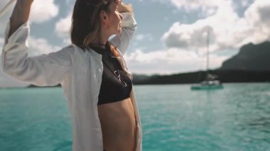 Turist tropikal bir denizde yelken açarken harika vakit geçiriyor. Arka planda bulanık bir yelkenliyle ufka bakıyor.