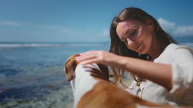 Bir kadın açık havada bir kayanın üzerinde oturuyor, yanında iki köpek var. Kadın köpeklerle etkileşim halindeyken rahat görünüyor. Kibar ve oynak görünüyorlar..