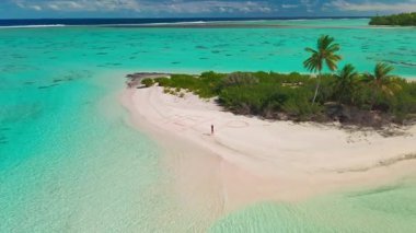Kadın, turkuvaz suları ve yemyeşil yemyeşil ile çevrili, terk edilmiş tropikal bir adanın kumlarına yardım yazıyor. Yalnızlık ve umut dolu sakin bir manzara yaratıyor.