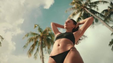 Genç kadın güzel bir sahilde sıcak güneşin ve tropikal esintinin tadını çıkarıyor. Kolları havada duruyor, teninde güneşi ve saçlarında rüzgarı hissediyor.